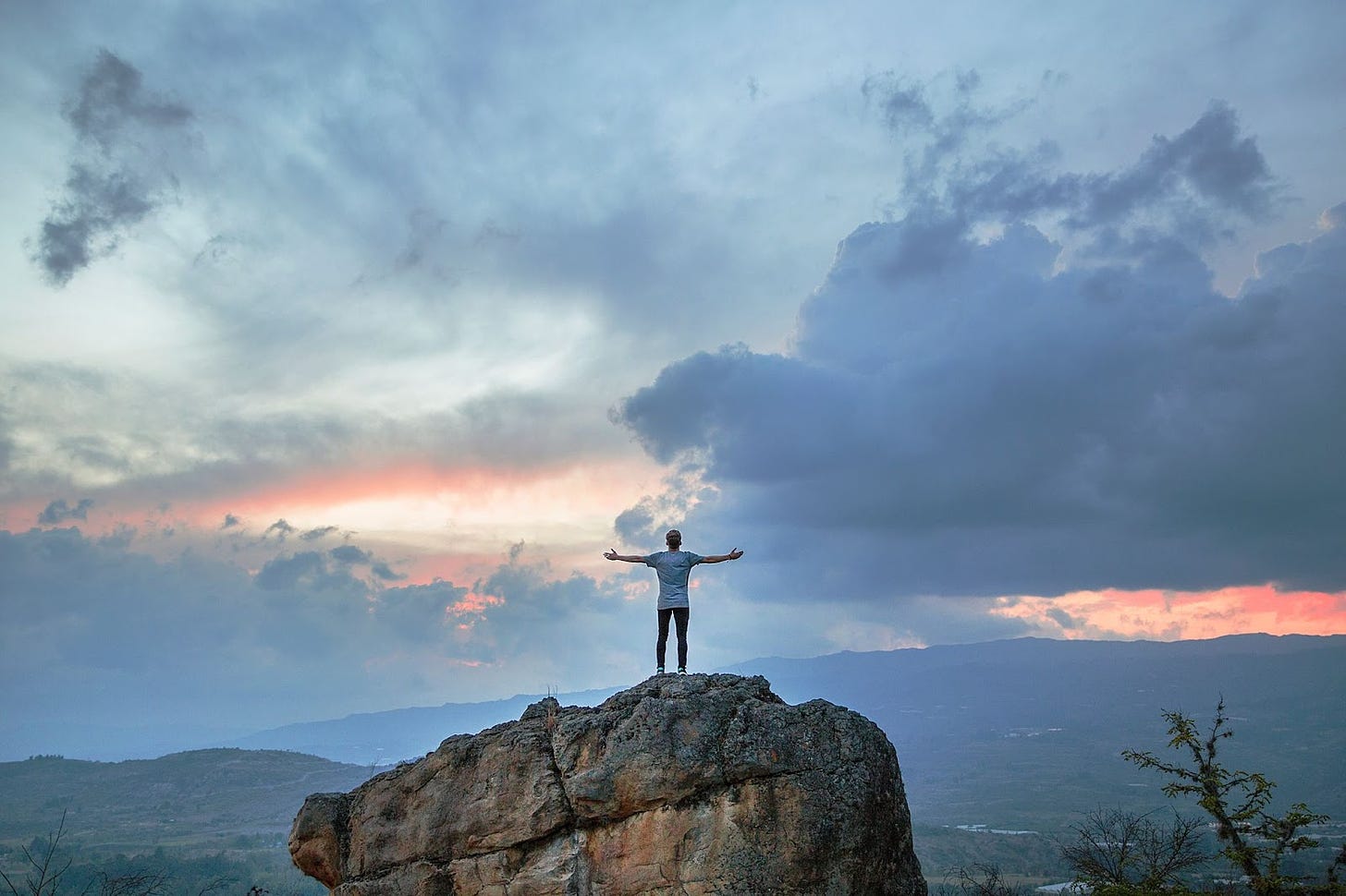 man standing on high rock arms open to a sunrise sky