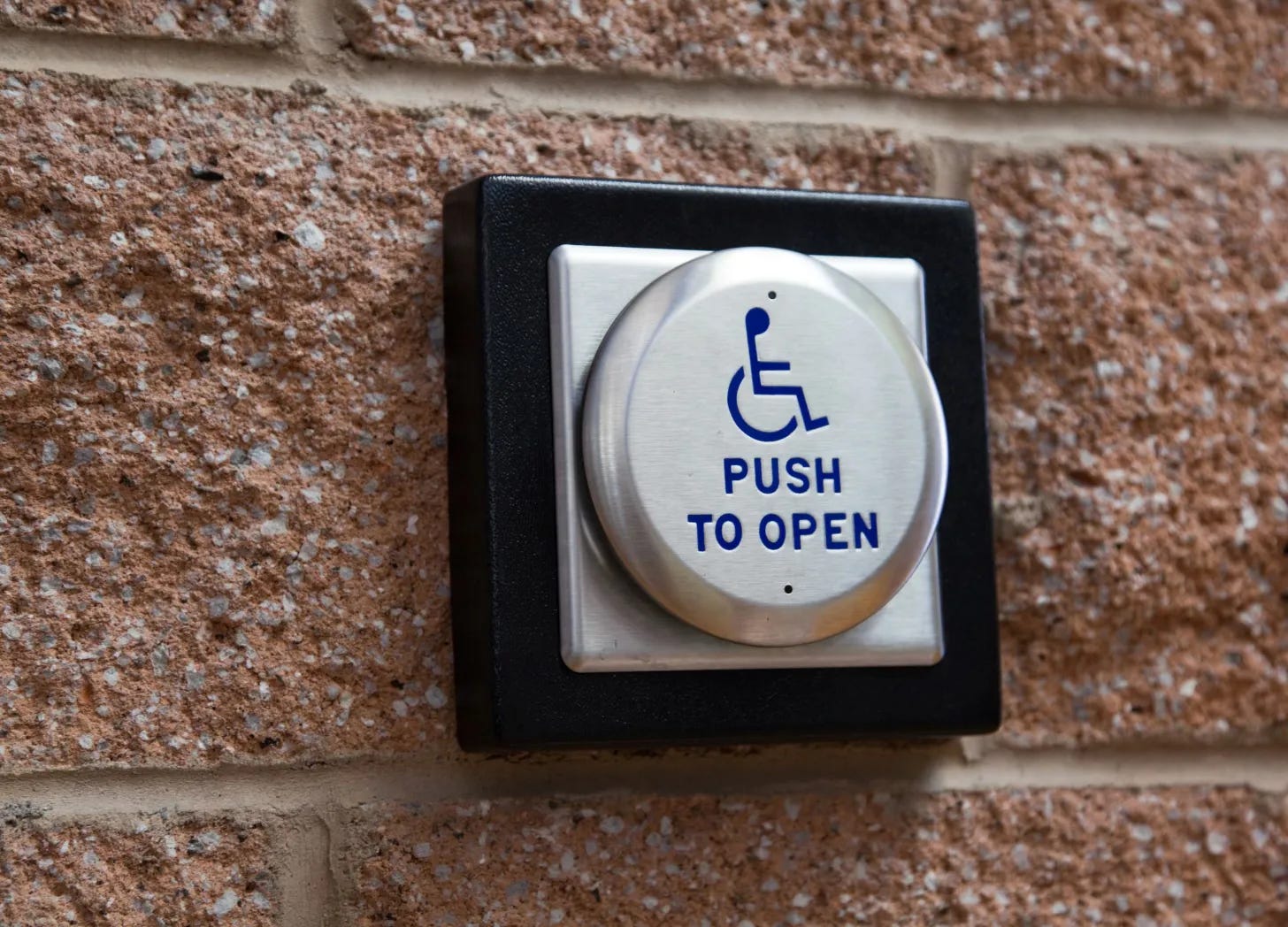 Push to open button mounted on a brick wall, with wheelchair symbol