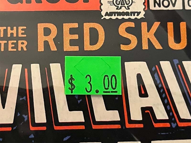 Green sticker on a comic book bag that shows a price of three dollars.