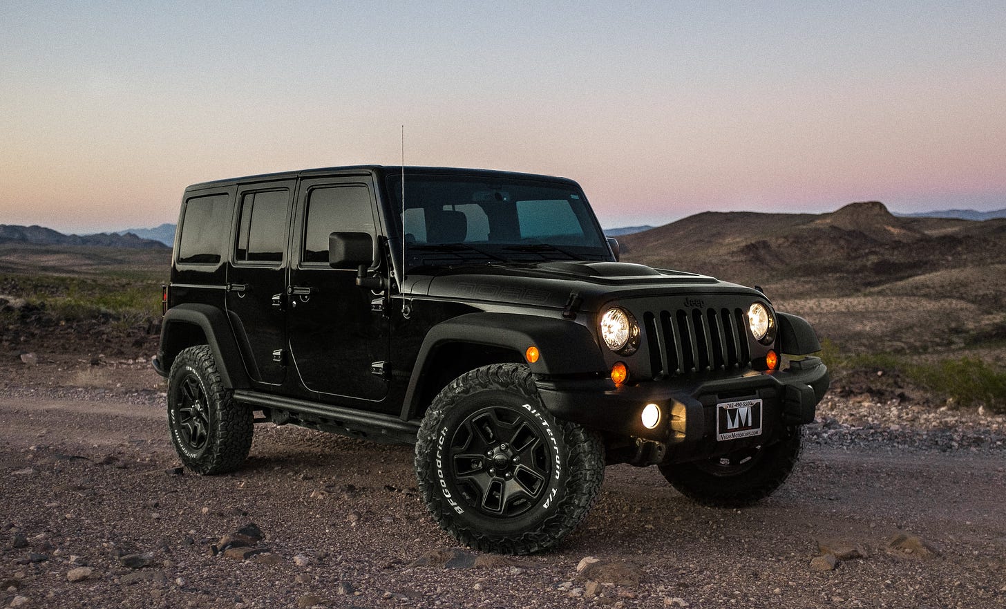 A black jeep set on a hilly dry landscape with a clear evening sky
