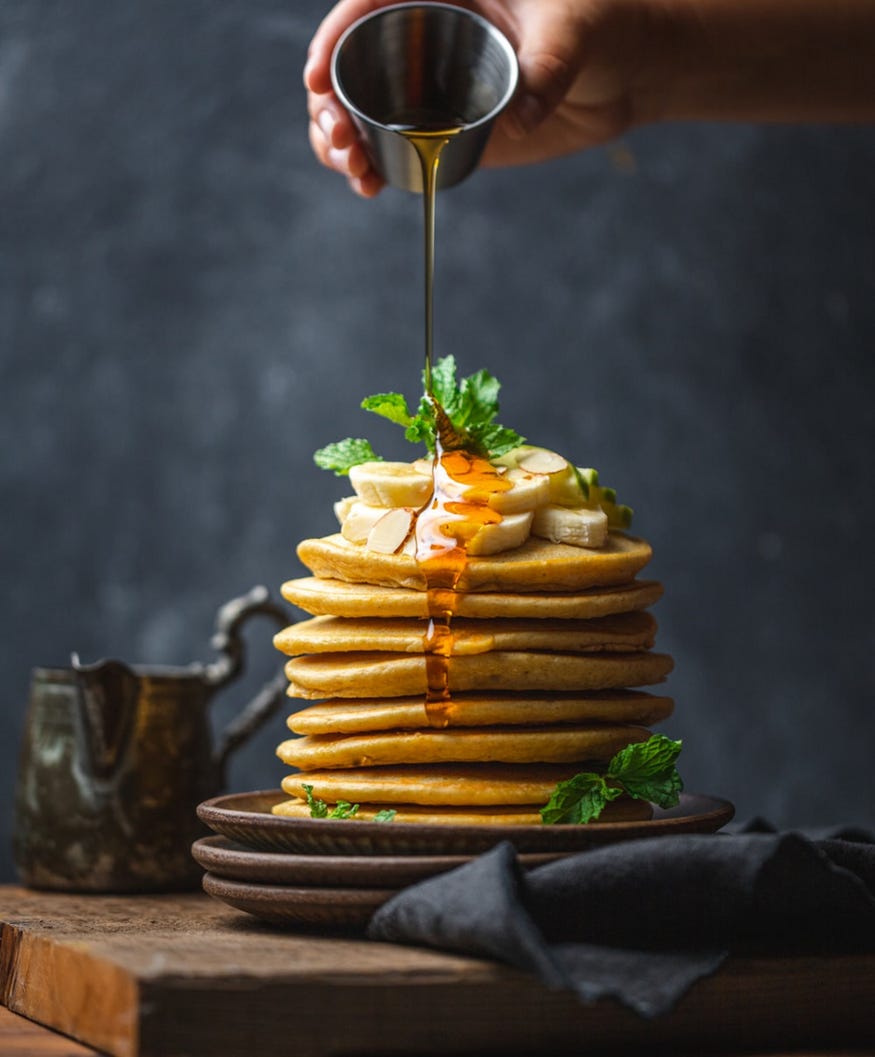 A pile of pancakes on a plate with a sliced banana on top drizzled with maple syrup