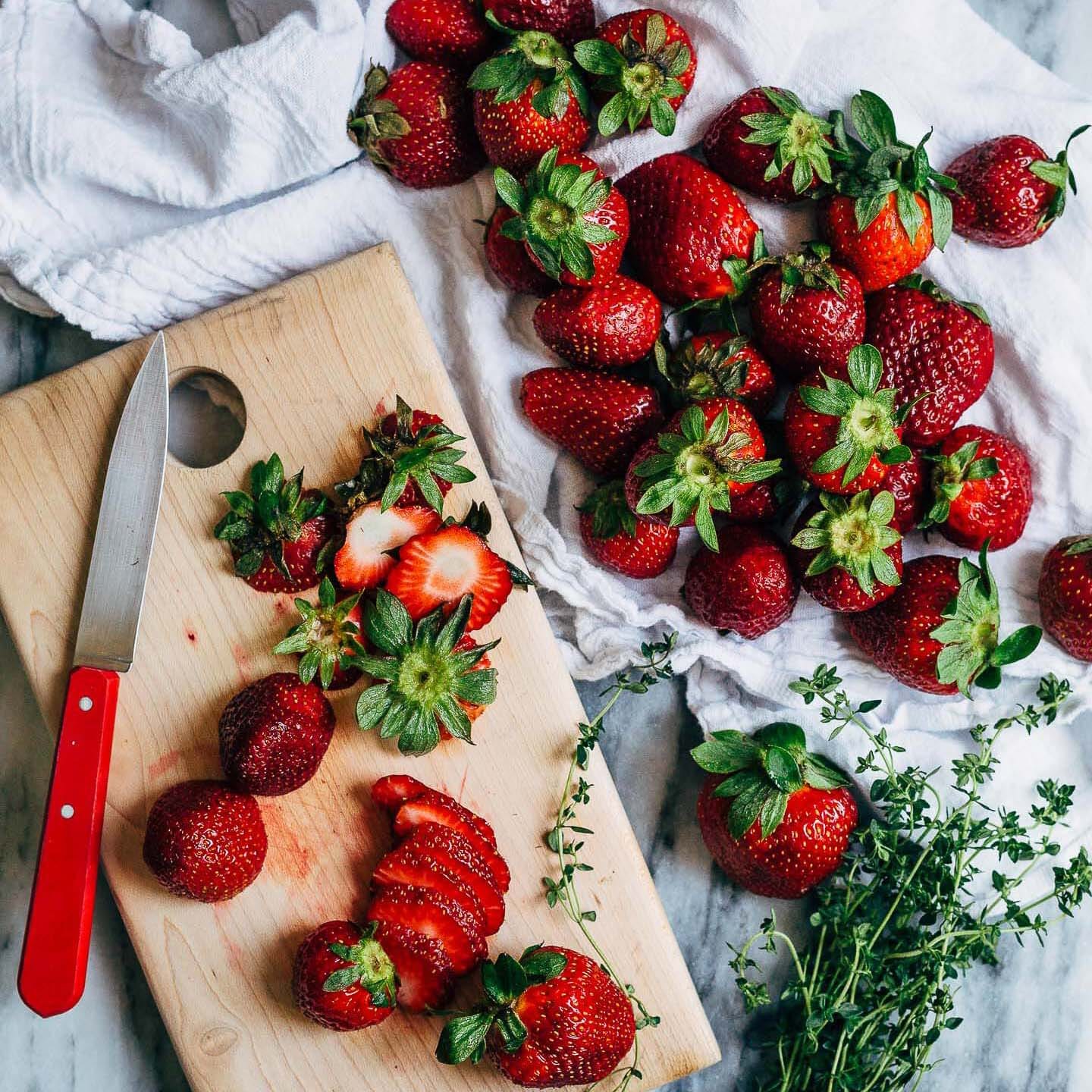 Sliced strawberries on a cutting board and little strawberries alongside 