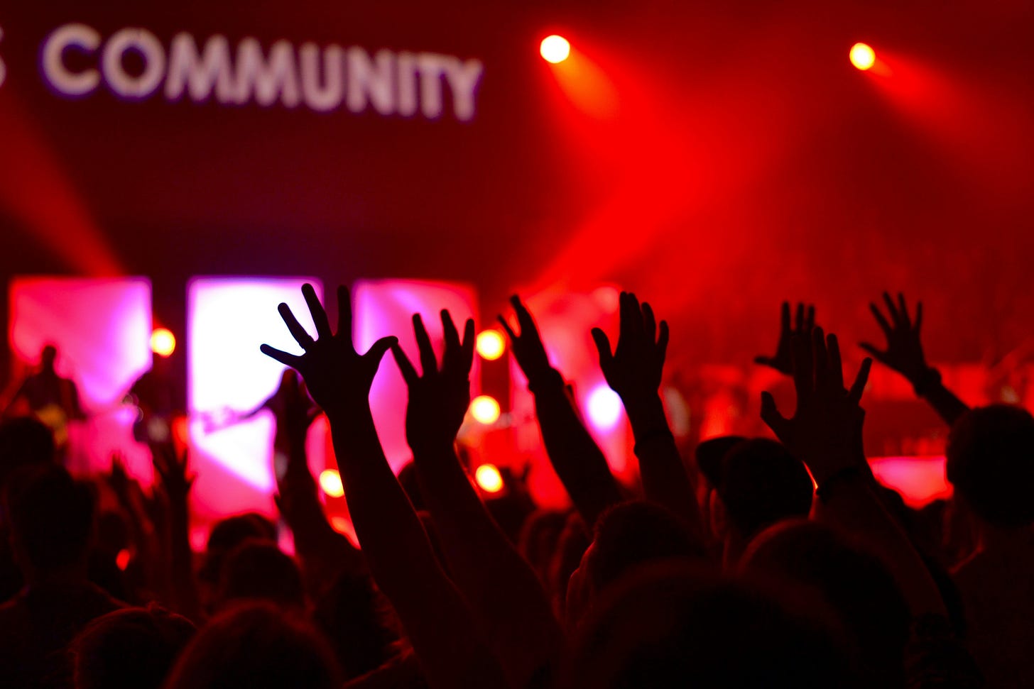 Red background with silouettes of raised hands and a sign in the distance that reads COMMUNITY