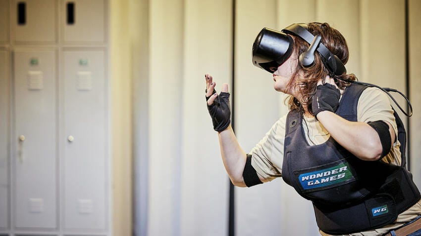 A woman in a VR headset and elbow pads stands in a locker room.