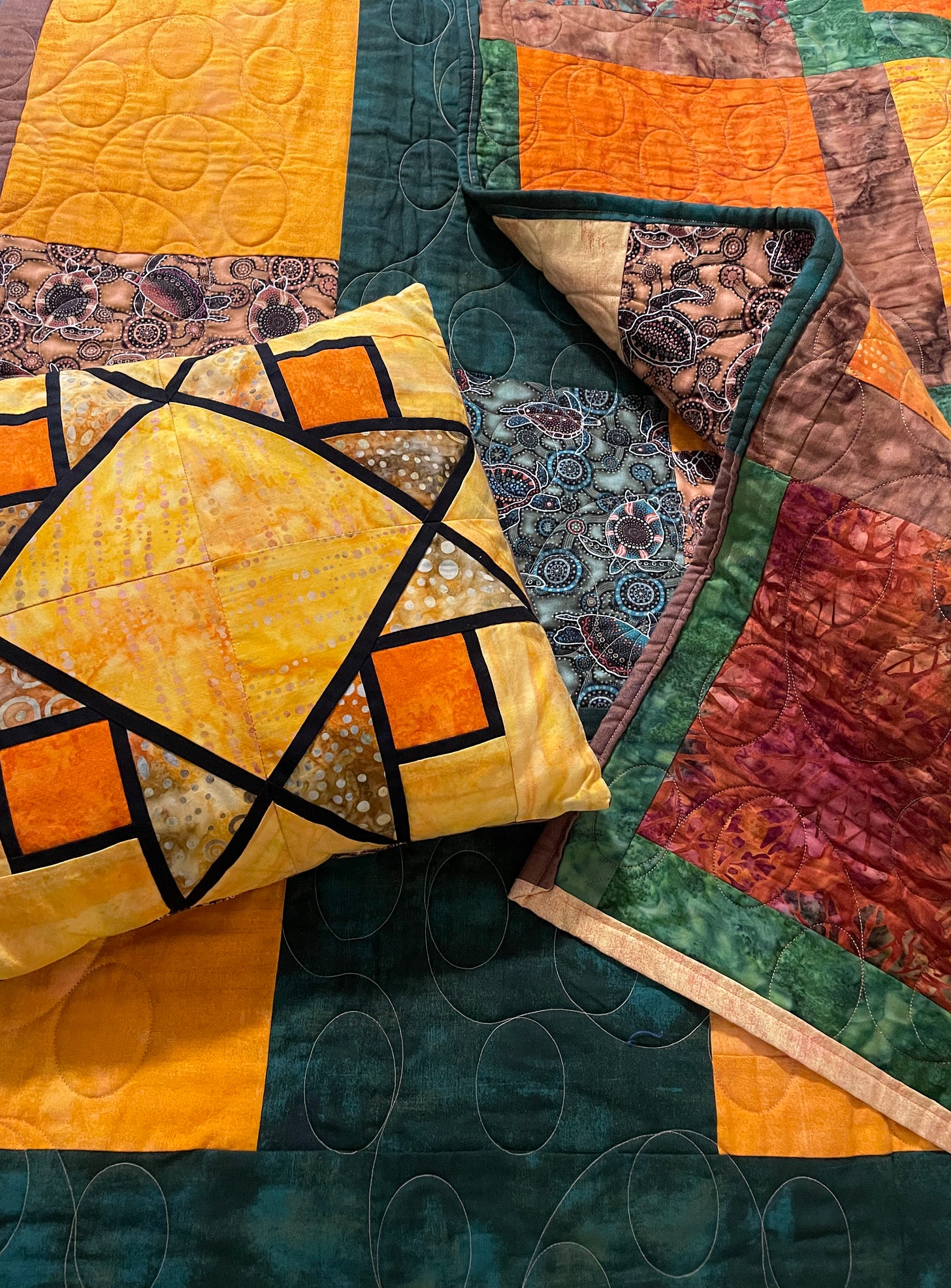 A quilt and pillow in yellows, oranges, and brown squares