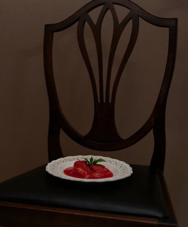 On a chair, a white plate with crushed tomatoes in the center and a sprig of basil.