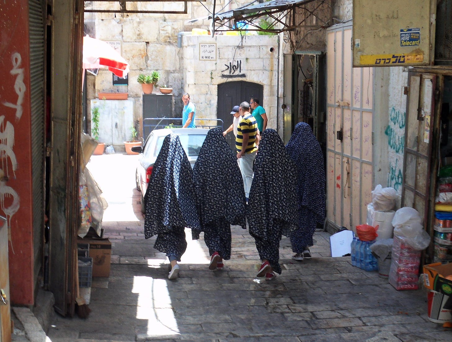 Four women in headscarves walk through an alleyway during a sunny day