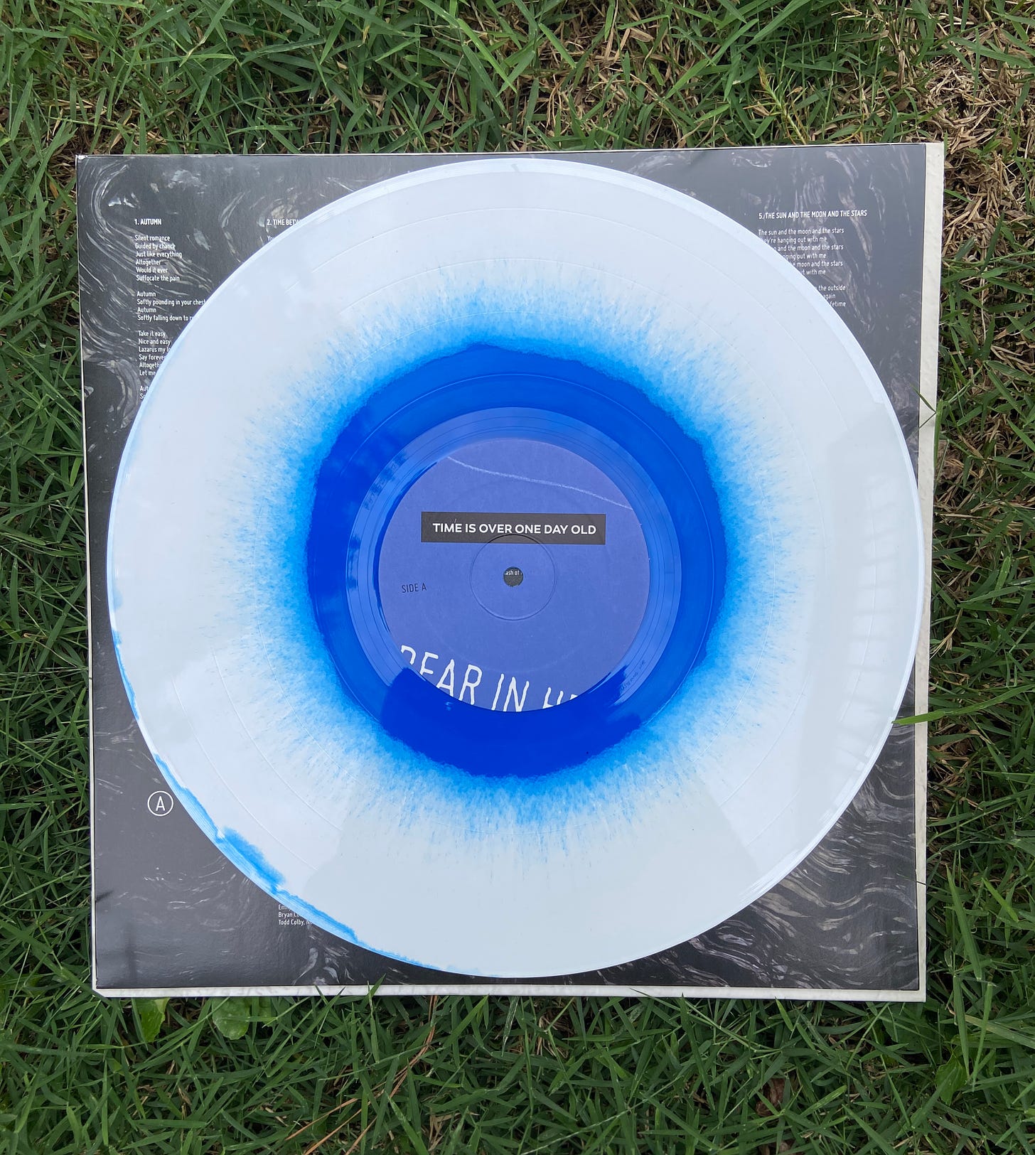 a vinyl of Bear in Heaven's fourth album Time is Over One Day Old sits on bright green grass. the record has a white and blue splatter design, and the inside jacket has a swirly black and white pattern.