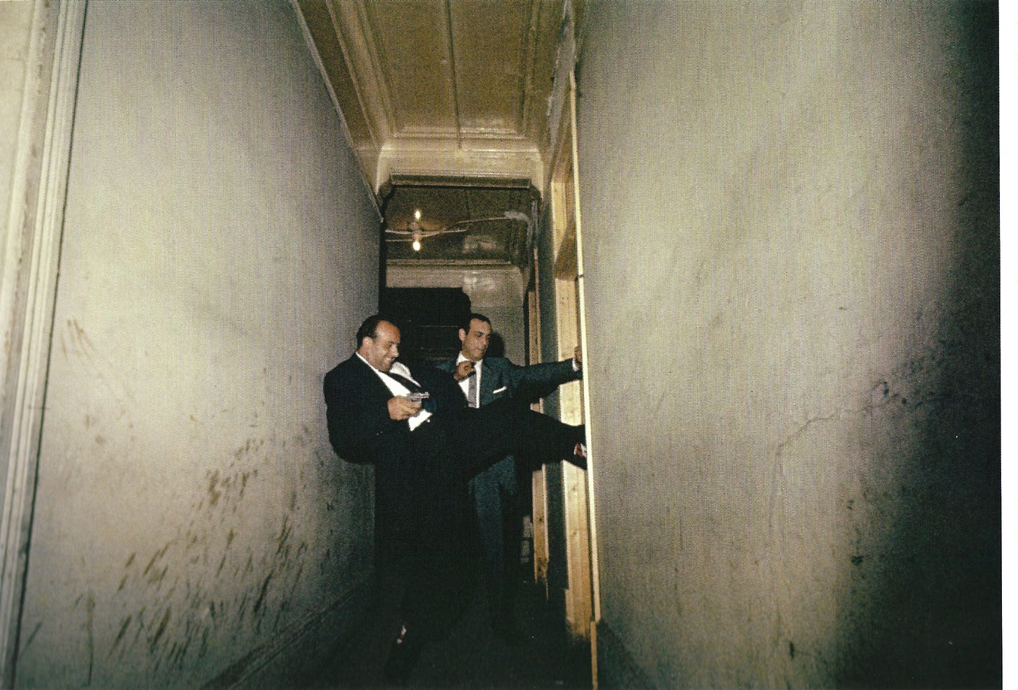 Two detectives, kicking in a door in a shabby hallway