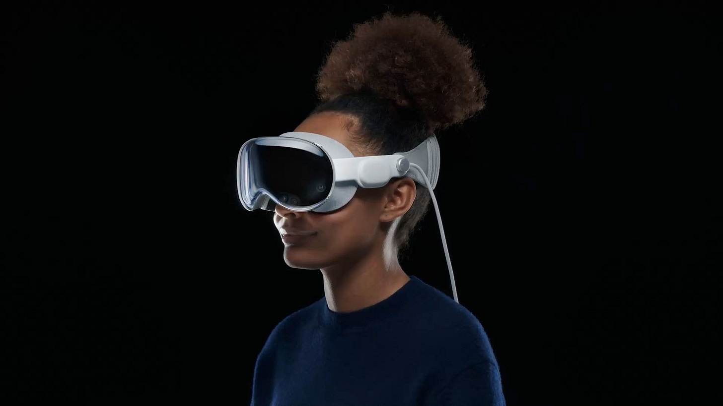 A user using Apple Vision Pro. The cord falling from beside the headset is for the battery which a user will place in their pocket. A user using Apple Vision Pro. The cord falling from beside the headset is for the battery which a user will place in their pocket.