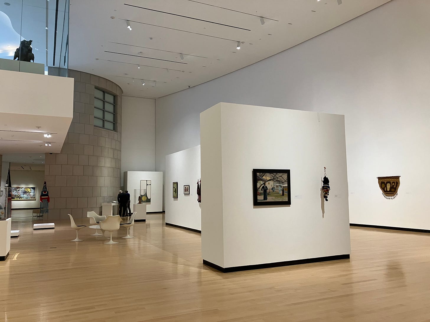 high ceilinged room partitioned by white walls with art, seating area with table and chairs, and overhanging balcony