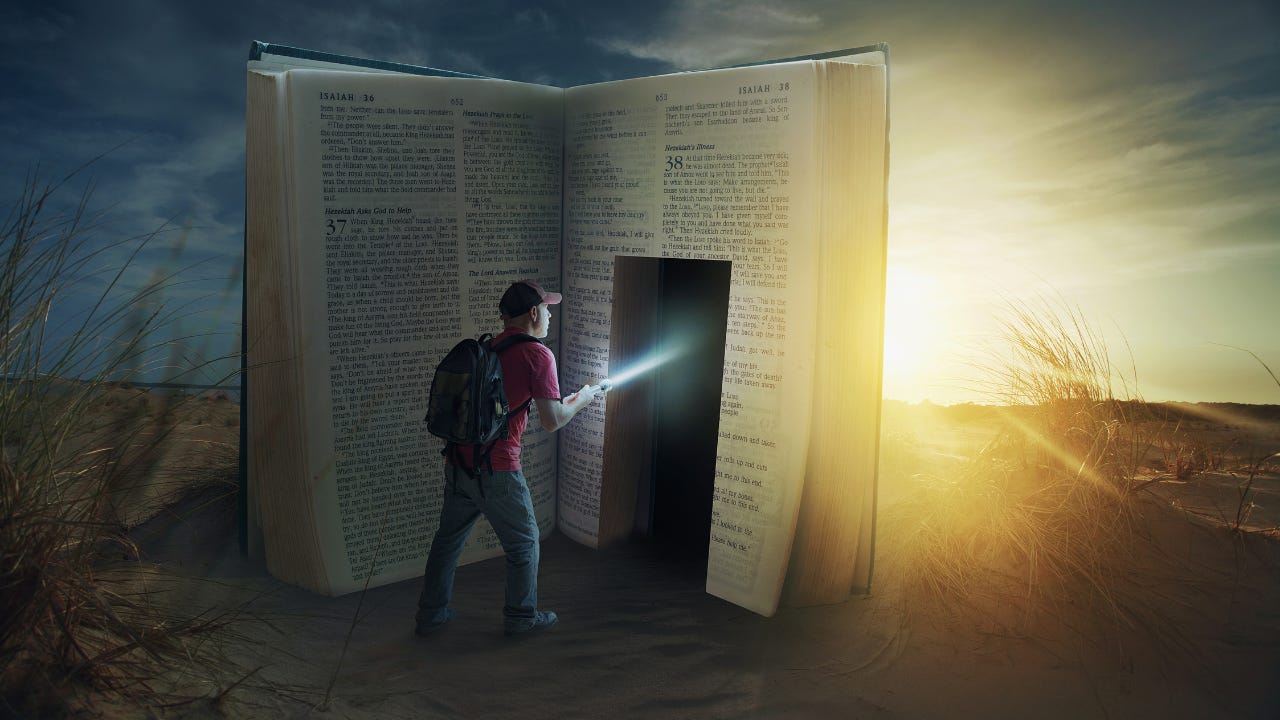 A man with a flashlight about to walk into a large copy of the Bible. 