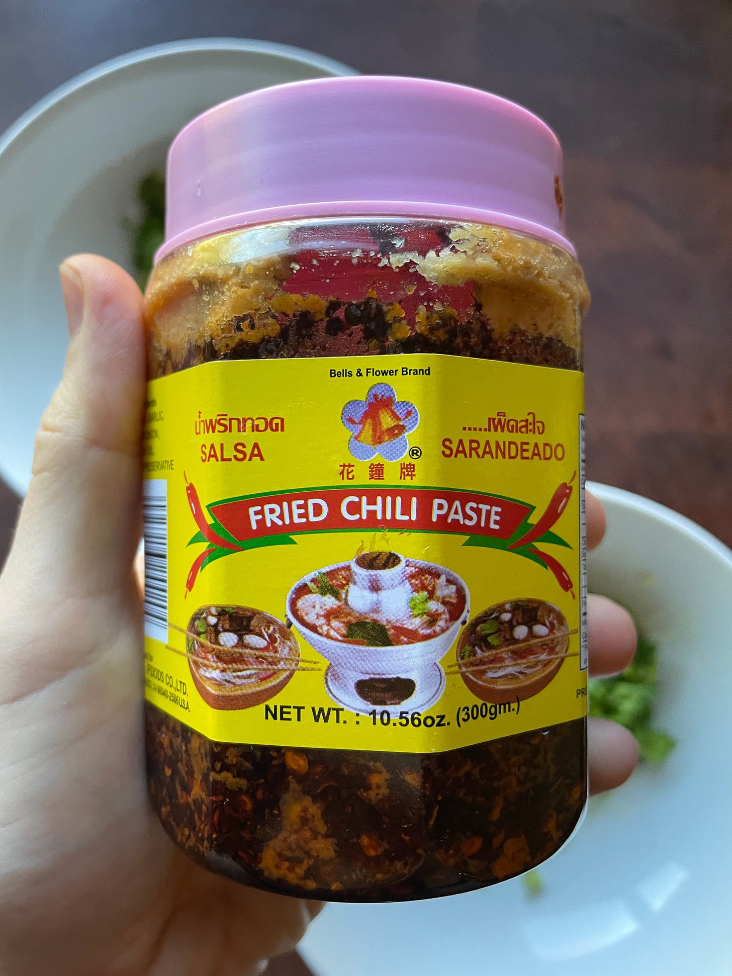 A hand holding a container of fried chili paste that has a yellow label and a pink lid