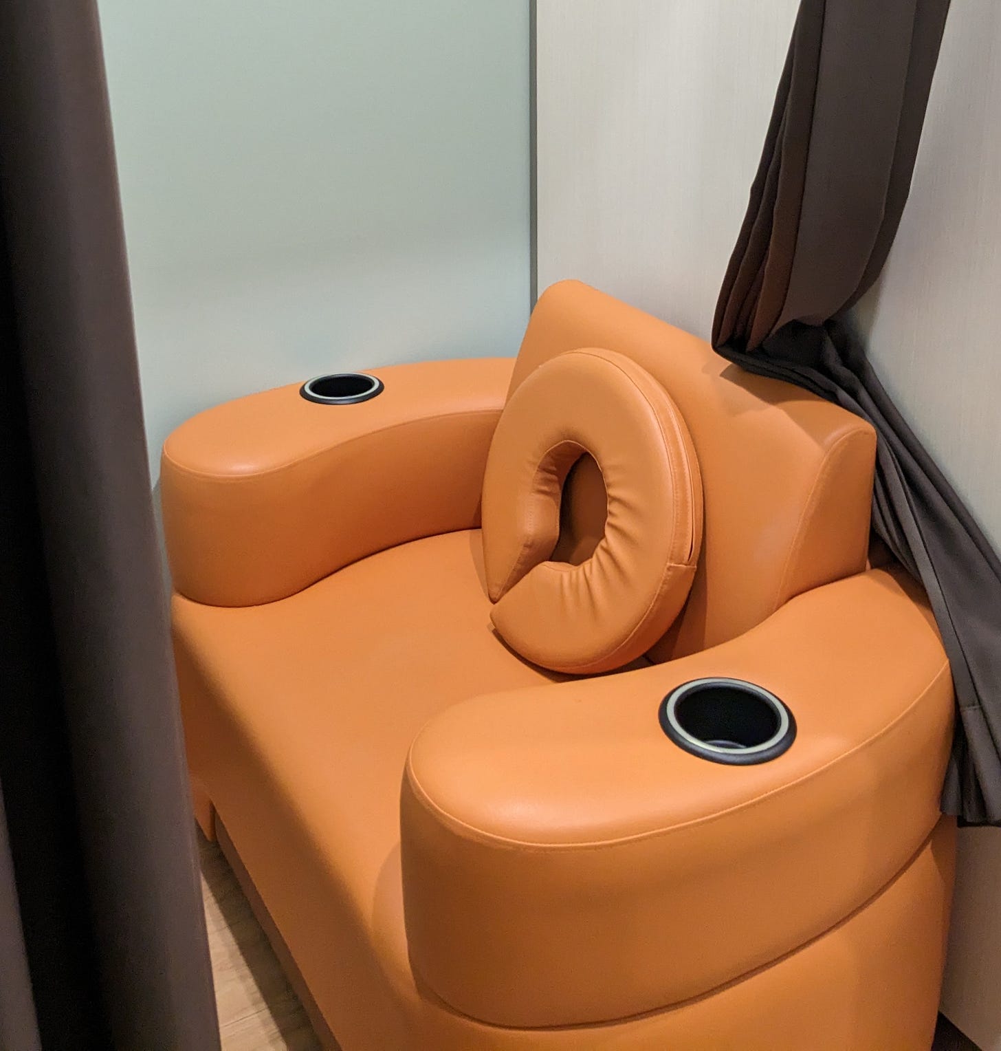 An wide, orange-colored leather seat with comfortable, wide arm berths and a doughnut pillow, with curtains surrounding the space -- able to be fully enclosed