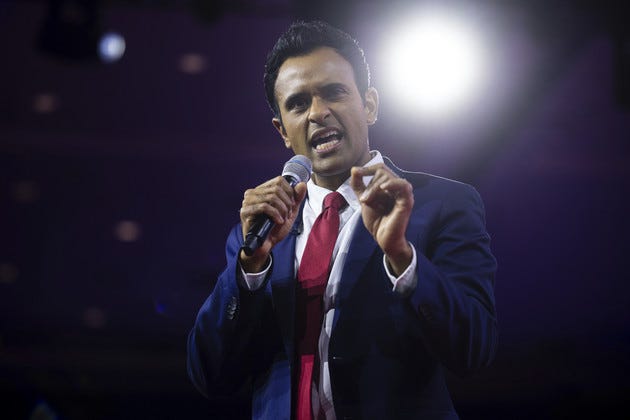 Vivek Ramaswamy speaking while holding a microphone, with a spotlight shining behind him.