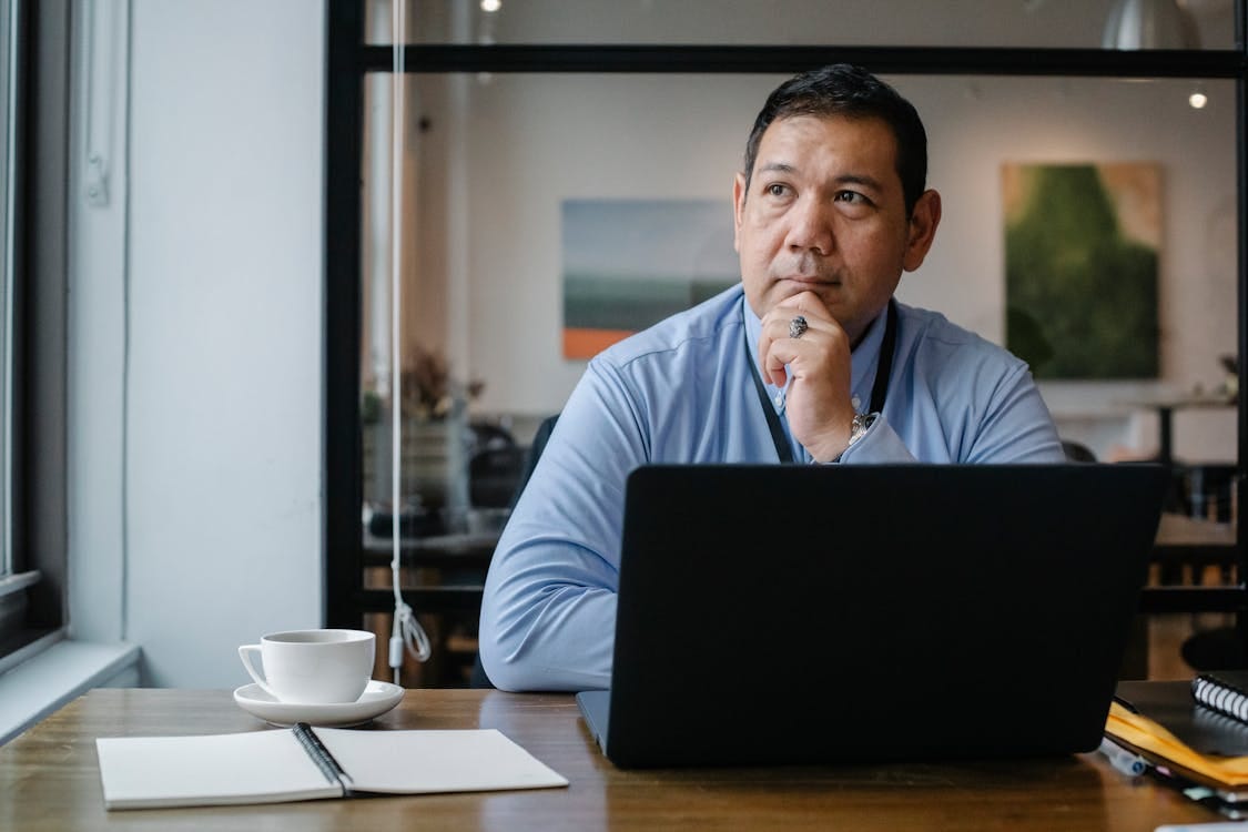 Free A businessman deep in thought while working on a laptop in a modern office setting. Stock Photo