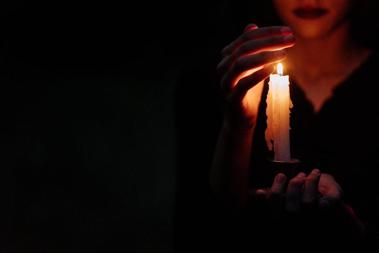 a person covering the lighted candle he is holding