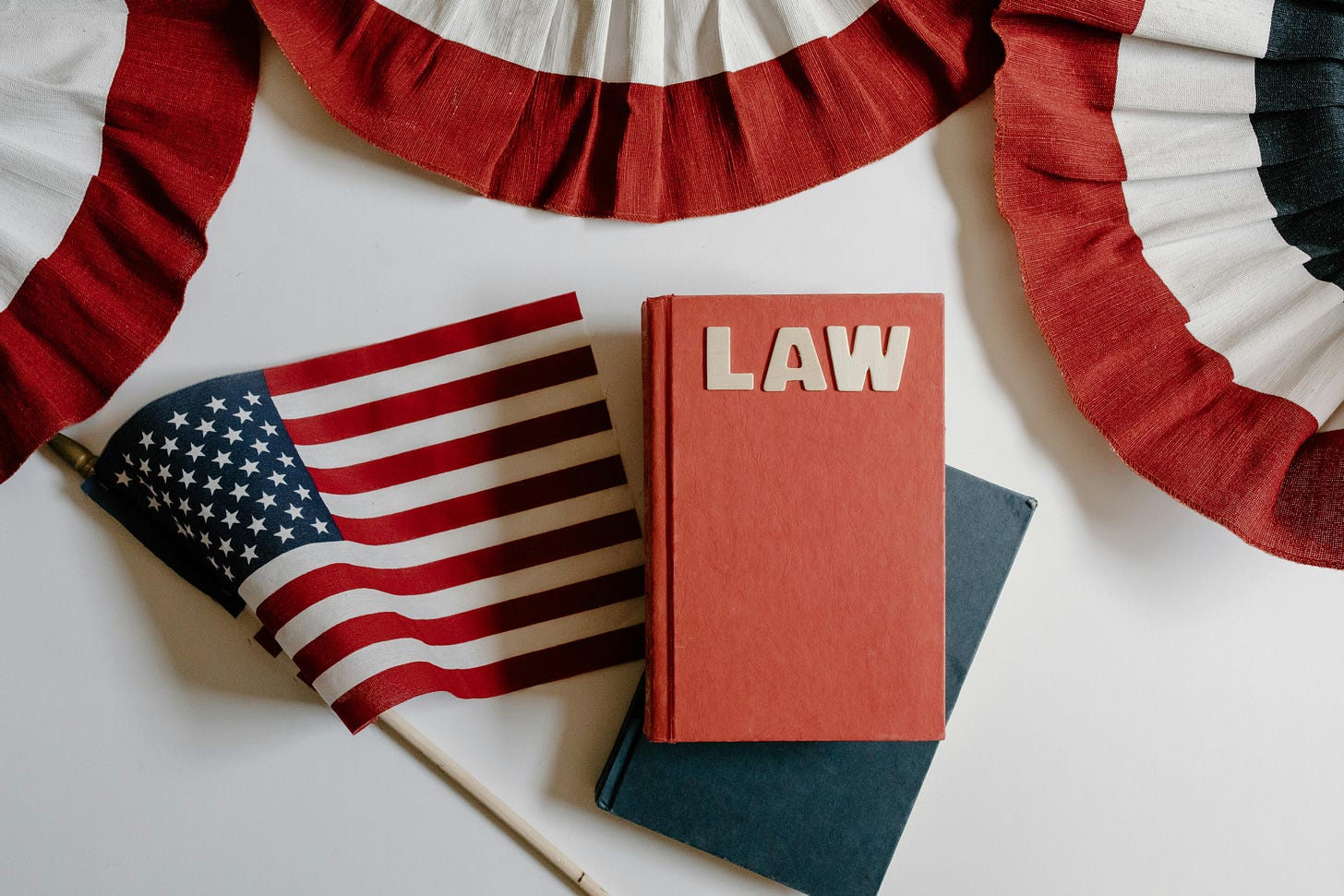 Each state in the USA has different laws. This image shows an American flag with a book that says “Law” on the cover.