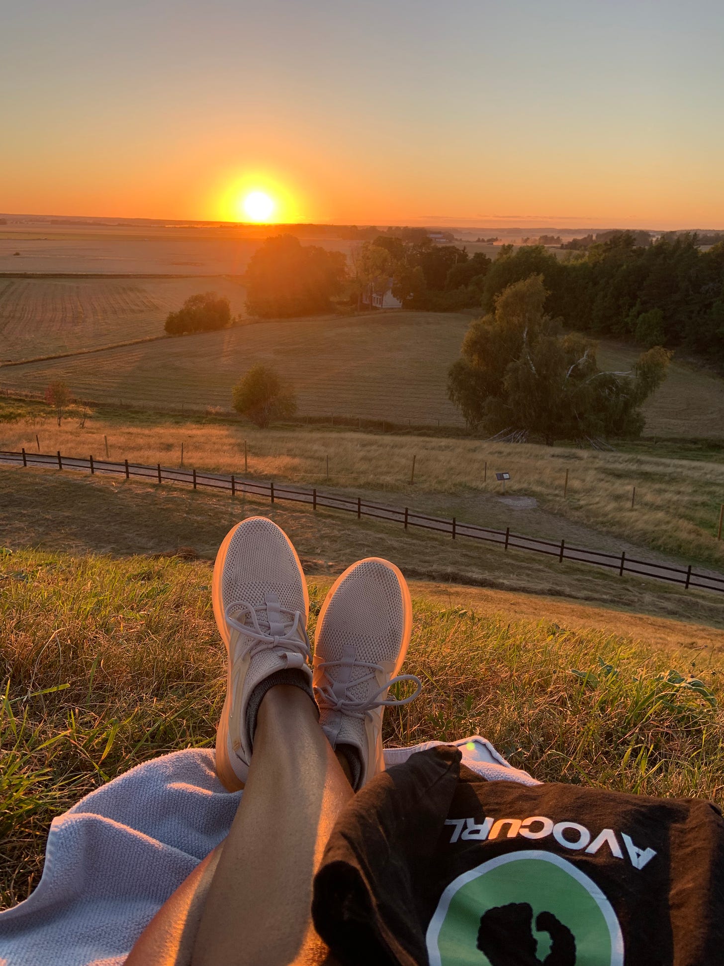 a black woman enjoys a yellow and orange sunset, while sitting legs crossed on top of a mound in Gamla Uppsala, Sweden
