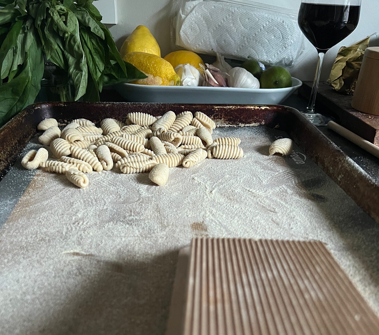 ridged cavatellli on a sheet pan in front of a wooden pasta rolling board