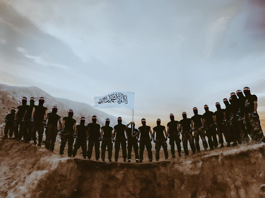 Taliban fighters standing with a flag in a mountainous region.