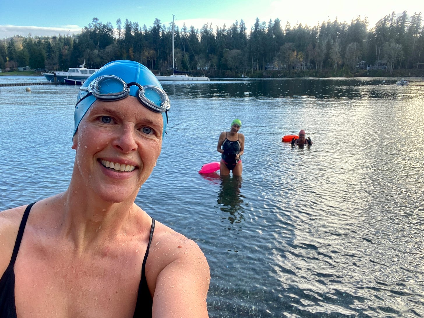 A photo, a selfie by a woman at the shore of the Puget Sound with two women in the water behind her.