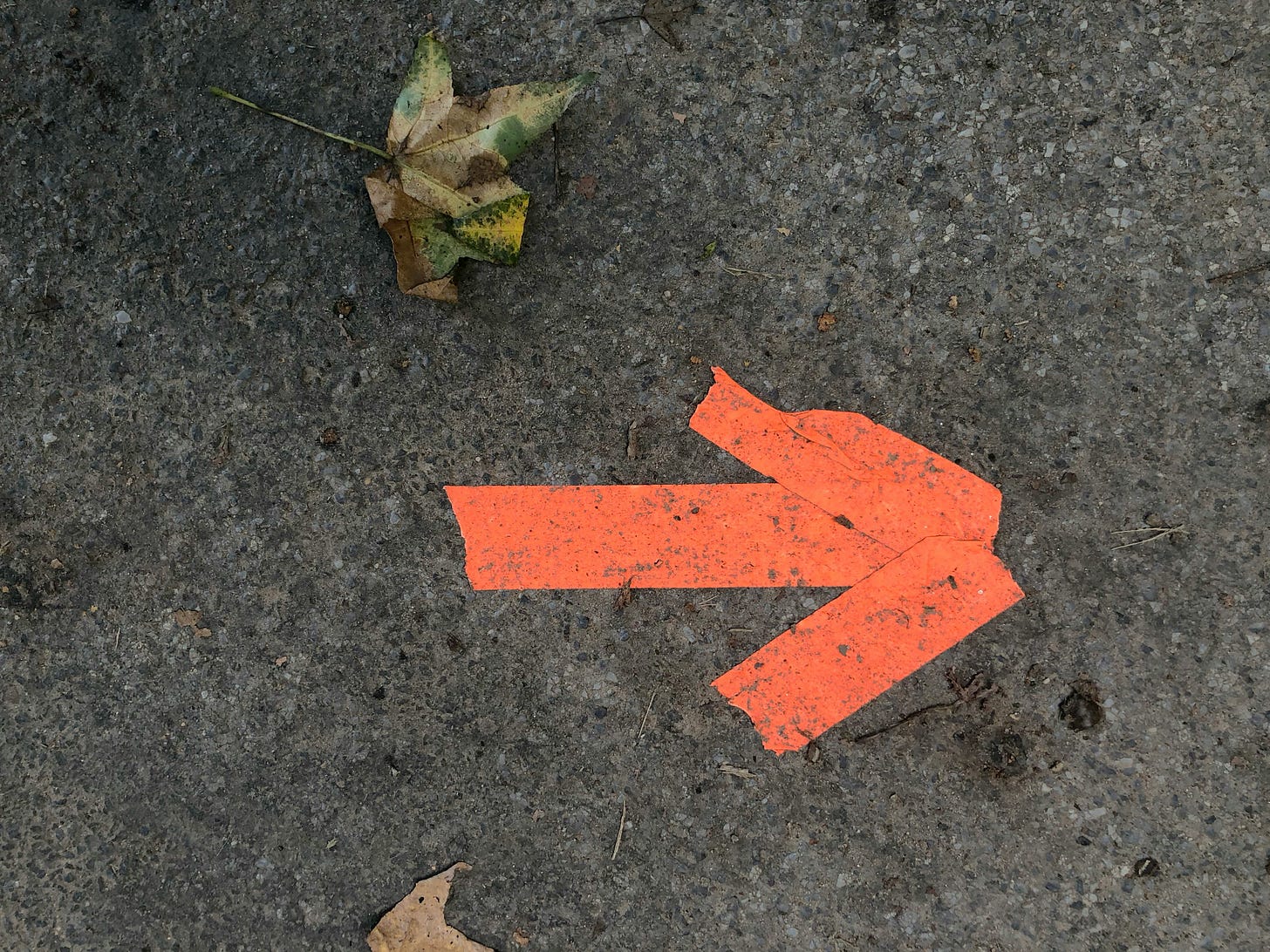 An orange arrow made of tape on a gray conrete sidewalk
