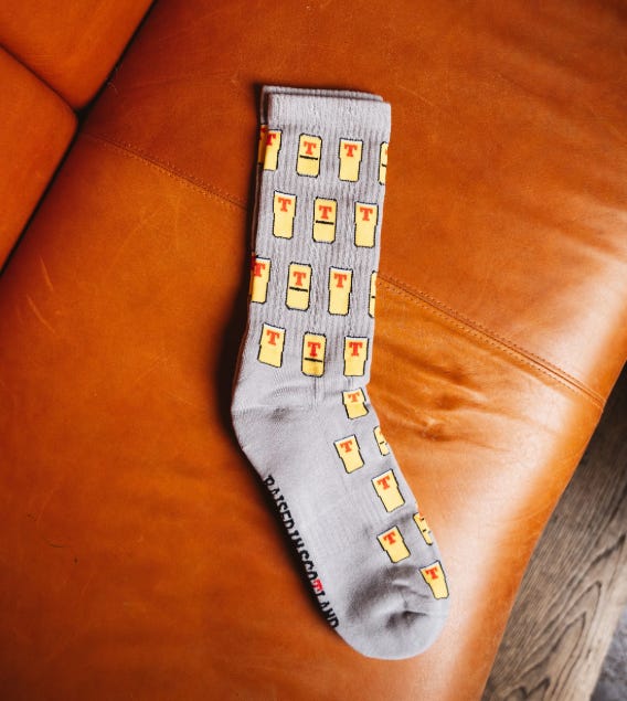 Light grey socks with little yellow Tennents pints all over in a repeating pattern, all with little red Ts on them. On the sole it says "Raised in Scotland."