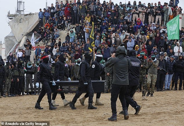Crowds of Hamas fighters and civilians watch on as the coffin of one of the hostages is carried to a waiting Red Cross vehicle on February 20