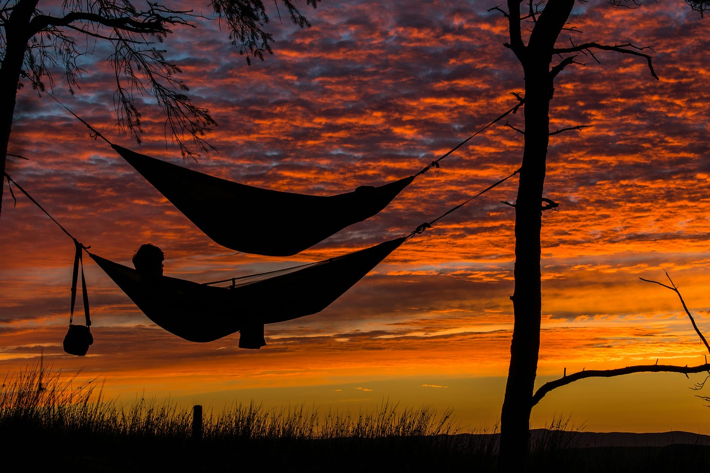 The silhouette of two hammocks set against a red and yellow sunset.