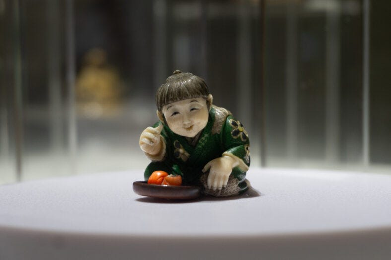 image of a japanese ivory netsuke, which is a tiny sculpture of a boy with a Daruma toy