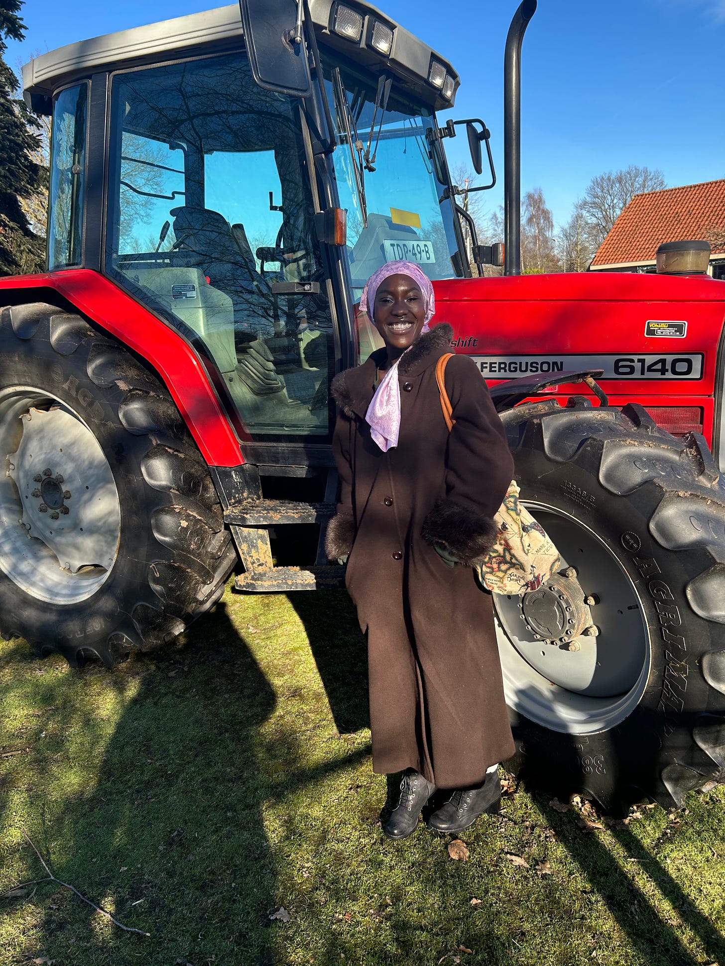 Ismatu is pictured standing in front of a large, bright red tractor 