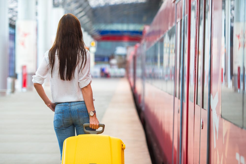 a woman with a suitcase standing on a platform at a station. the train has its doors closed