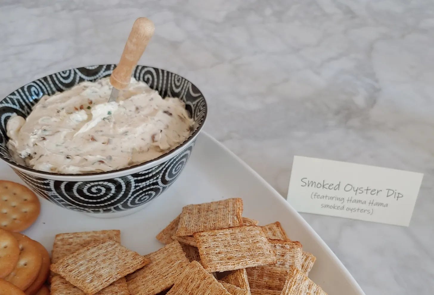 A bowl of smoked oyster dip on a platter of crackers.