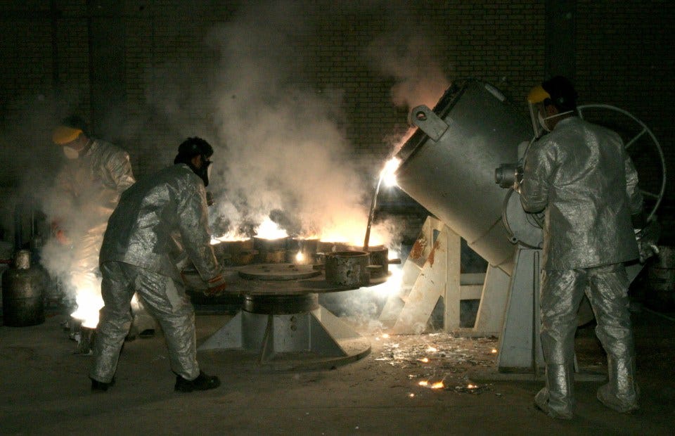 Technicians pouring molten metal at a uranium processing site.