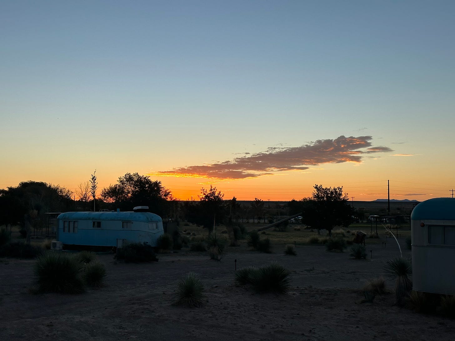 A sunset fades from blue to orange, with a right-leaning plume of clouds in the distance, over a trailer in Marfa, Texas.