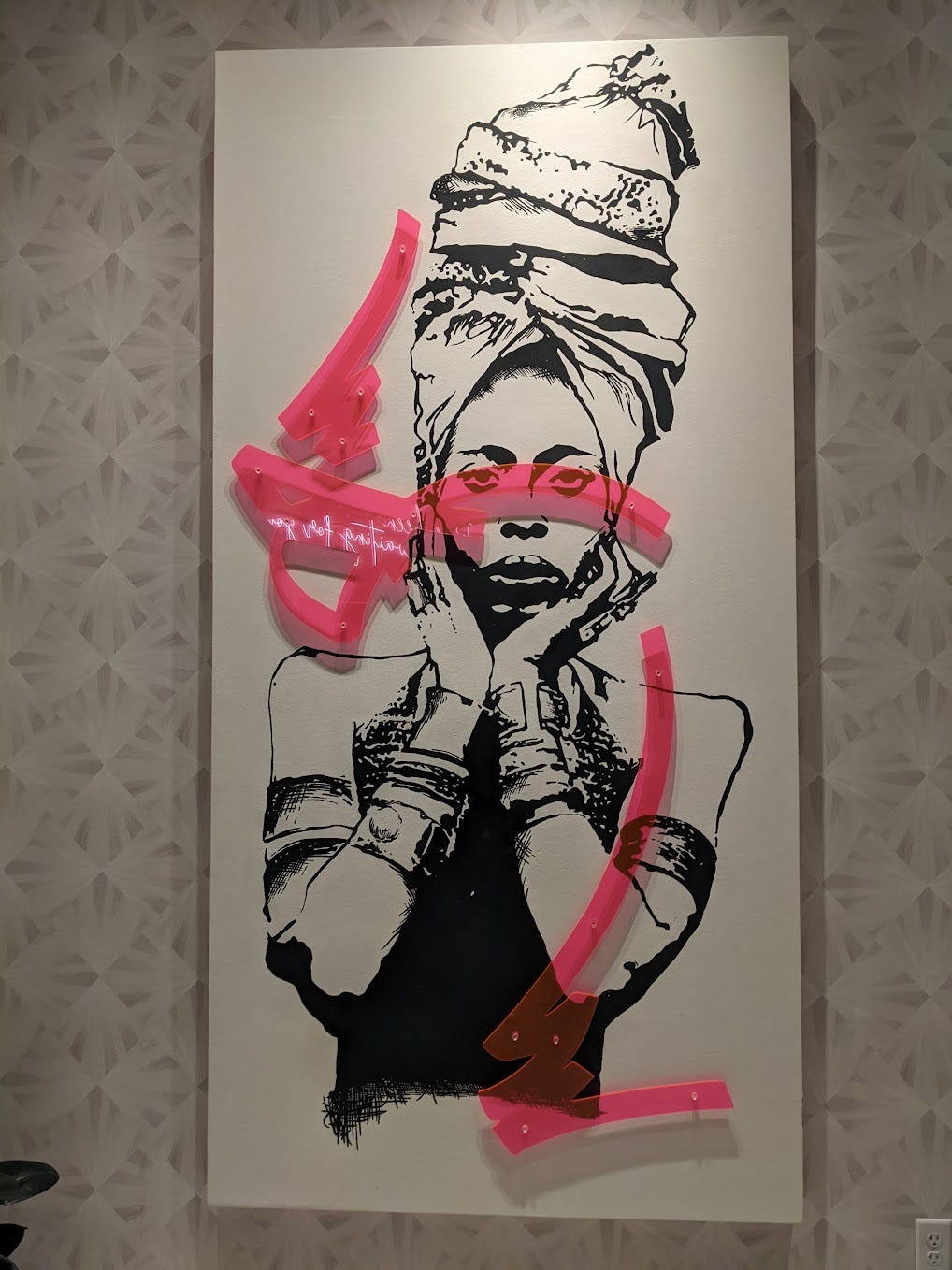 black and white print of erykah badu, on wall, with bright pink abstract painted squiggle. erykah has her head wrap on and her hands cupping her face.