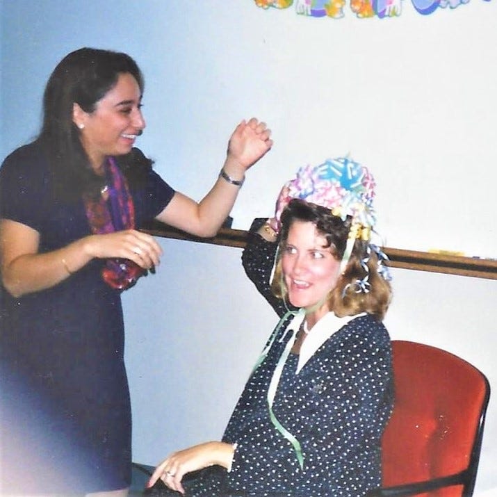 Young woman helps the guest of honor straighten the bow hat placed on her head at a baby shower