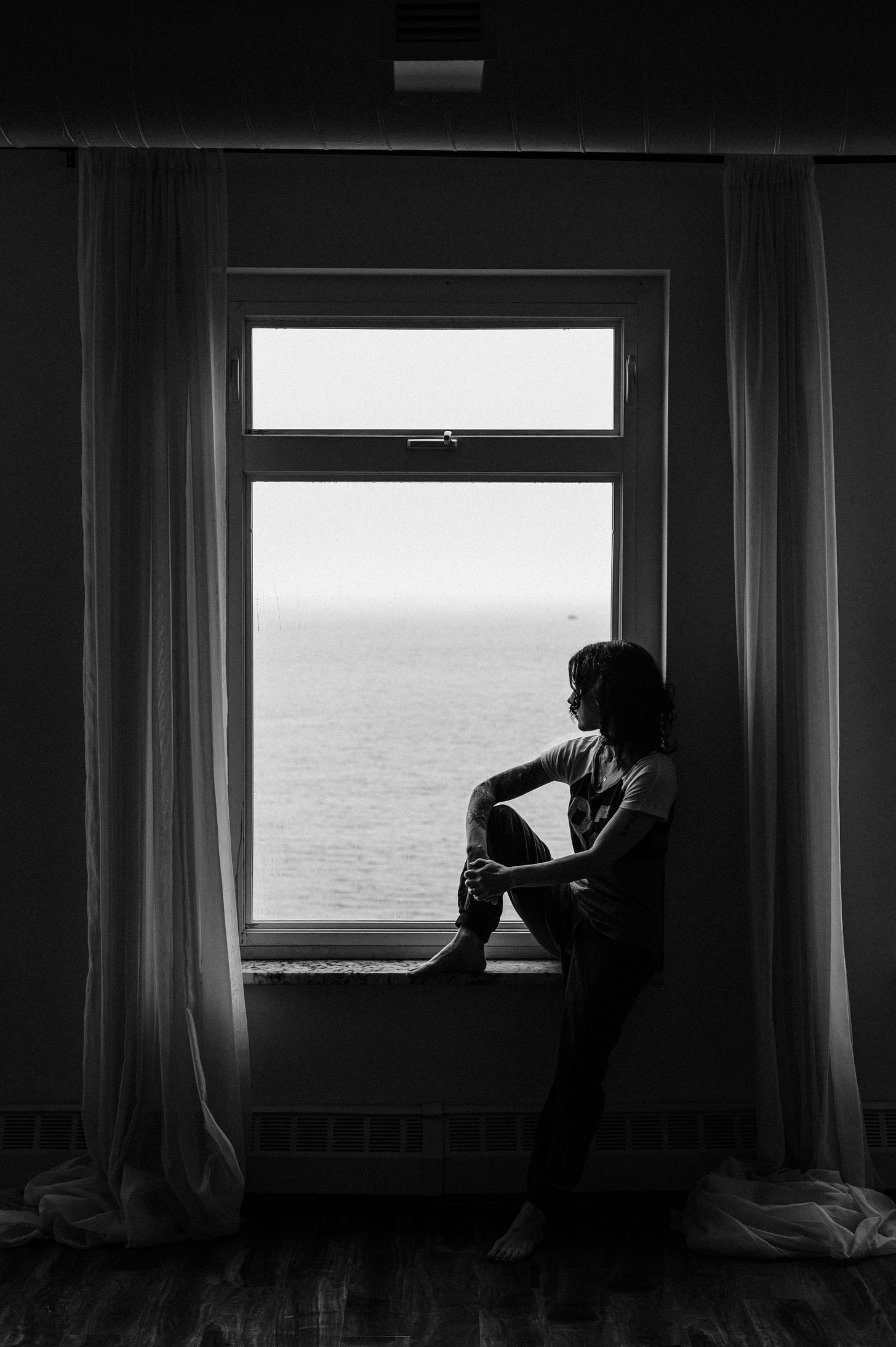 Author seated on large window sill looking out at the water