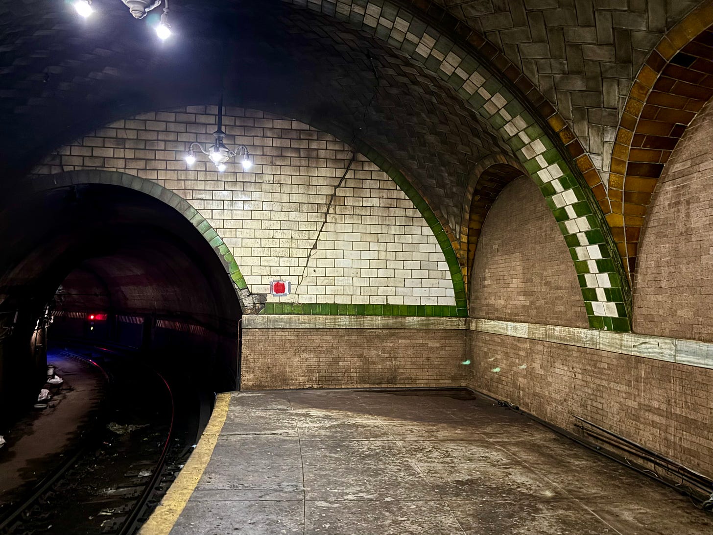The far edge of the subway platform. Green and amber tiles meet at the corners of the vaulted arches.