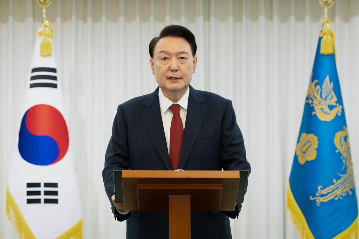 A person speaks at a lectern as flags are seen behind them.