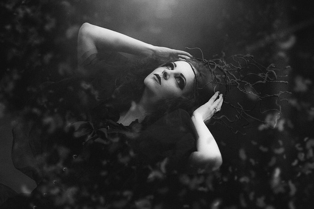 A gothic woman in a dark forest peering up at the night sky