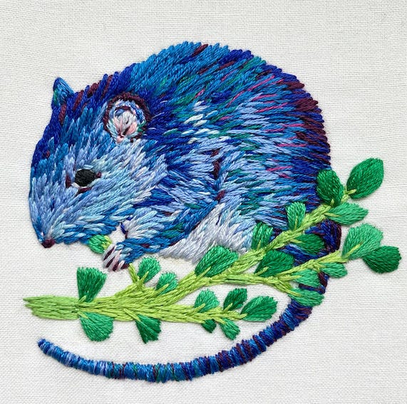 a small rat embroidered in shades of blue, eating a stalk of green purslane