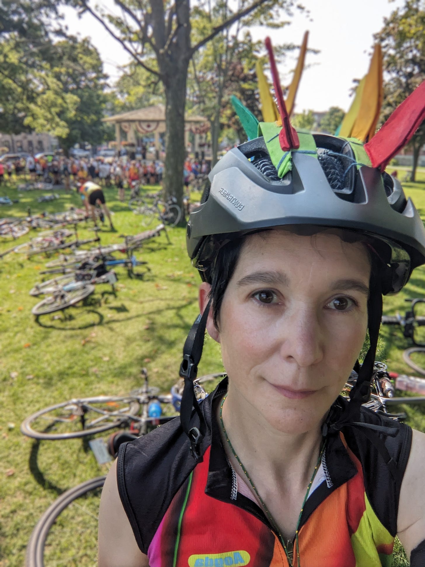 A light-skinned person in a black bike helmet stands in the foreground. In the background, a mass of bikes and a crowd.