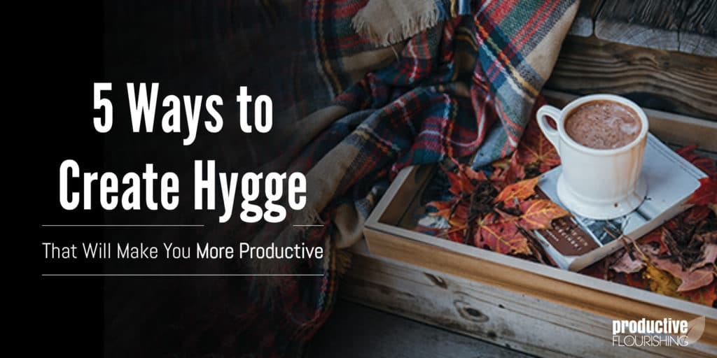 Photo of a hot chocolate in a mug, sitting on top of a book and fall leaves. Text Overlay: 5 Ways to Create Hygge That Will Make You More Productive.