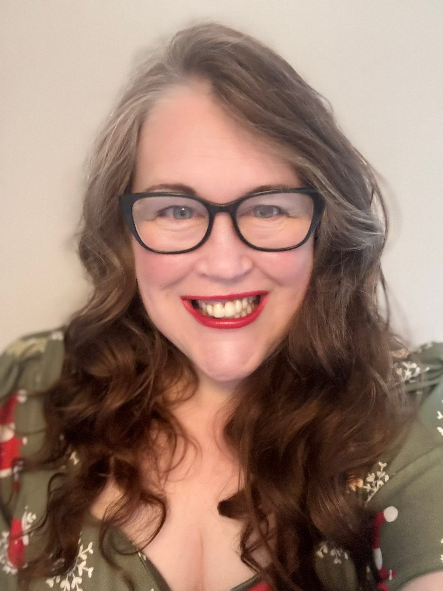 Photo of Yolanda Barker, Smily face with red lipstick on.  She has white skin,plump, long brown/grey hair that is curled.  She is wearing a green dress with 