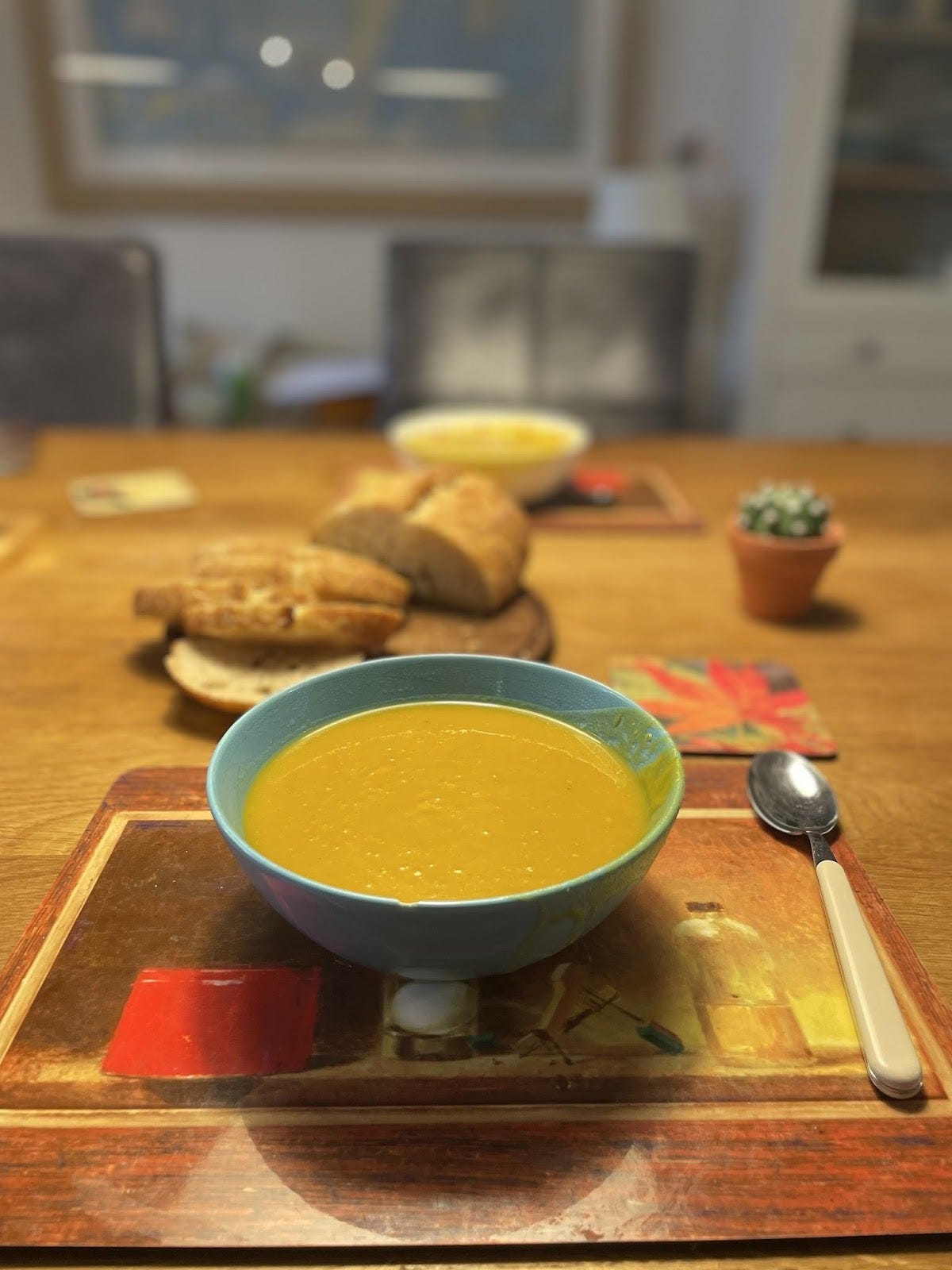  Bowl of soup on the table with bread behind it and another bowl across the table.