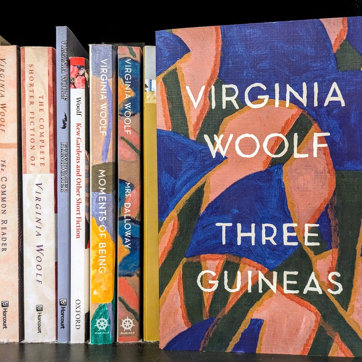 Partial view of a bookshelf with spines of books by Virginia Woolf, with the cover of Three Guineas facing forward.