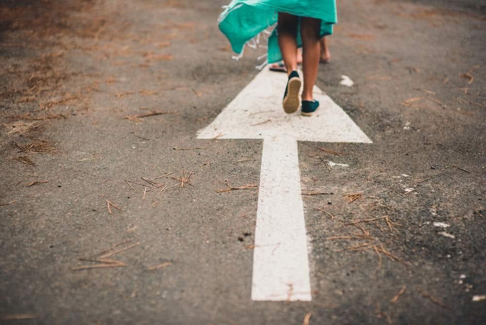 Photo of a child running up a street onto which is painting a big white "go this way" arrow.