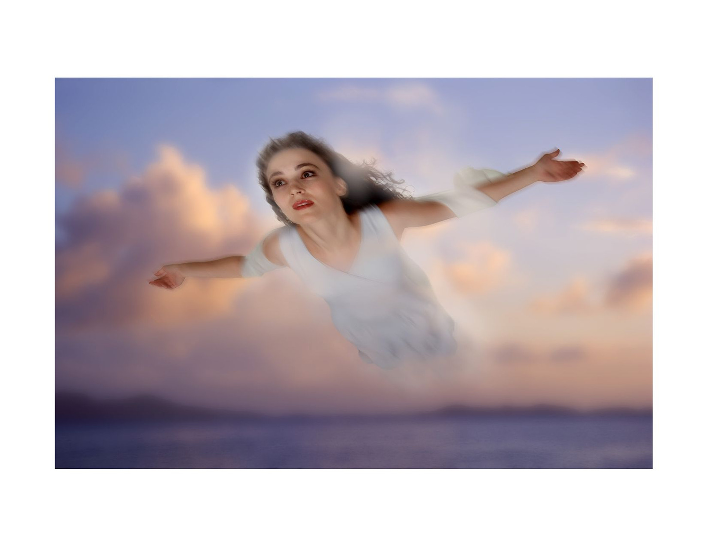 A woman soars through the air in a white gown, a blurry sunset in clouds over an ocean behind her.